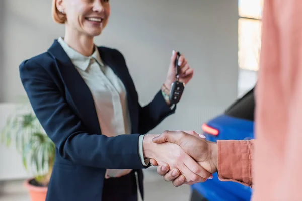 Partial view of car dealer holding key while shaking hands with blurred african american client — Stock Photo