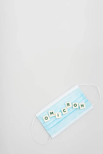 Top view of medical mask and white cubes with omicron lettering on grey background with copy space — Stockfoto