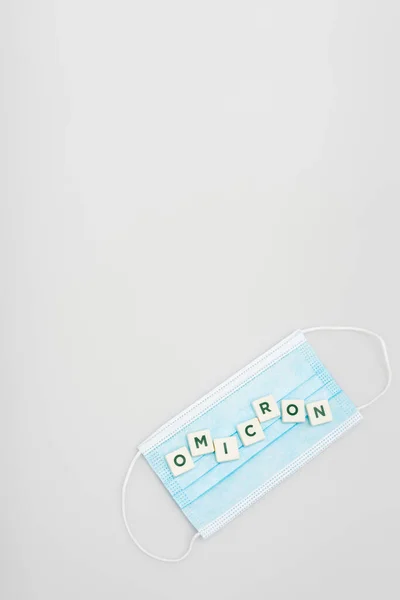 Top view of medical mask and white cubes with omicron lettering on grey background with copy space — Stock Photo