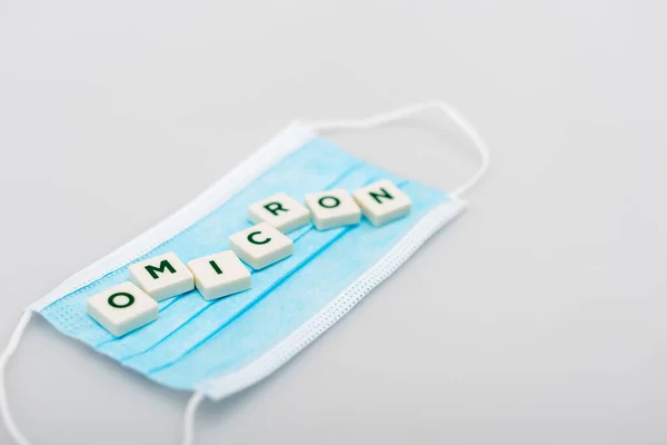 White cubes with omicron lettering on medical mask on grey background — Stock Photo