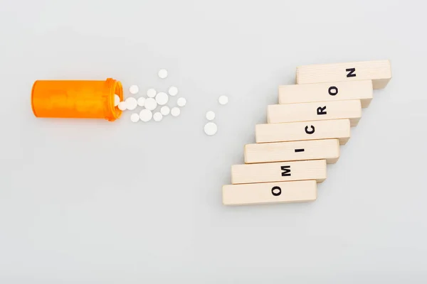 Top view of container and pills near wooden bricks with omicron lettering on grey background — Stock Photo