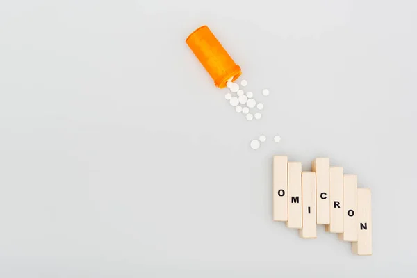 Top view of pills and wooden bricks with omicron lettering on grey background — стоковое фото