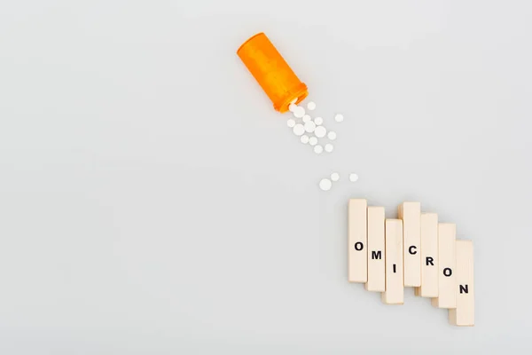 Top view of pills and wooden bricks with omicron lettering on grey background — Stockfoto