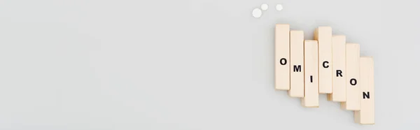 Top view of wooden bricks with omicron lettering near pills on grey background, banner — Fotografia de Stock