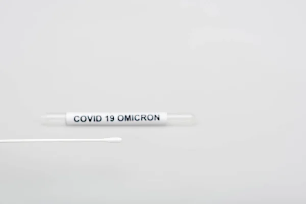 Swab test near blurred covid-19 omicron test tube on grey background — Stock Photo