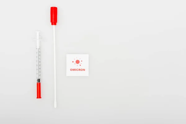 Top view of card with omicron lettering and bacteria icon near swab test and syringe on grey background — Stockfoto