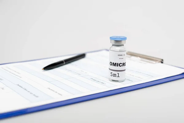 Вакцина проти омікрона ковадла-19 біля буфера з медичною карткою та ручкою на сірому фоні — стокове фото