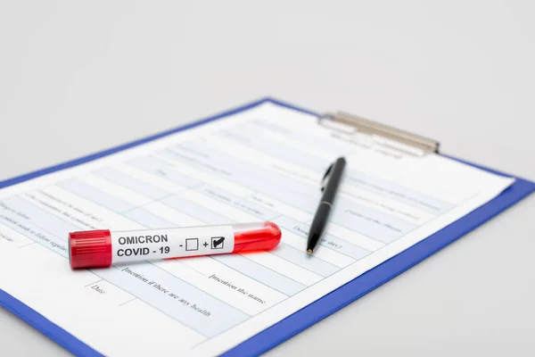 Clipboard with medical card, covid-19 omicron variant test tube and pen on gray background — Stock Photo