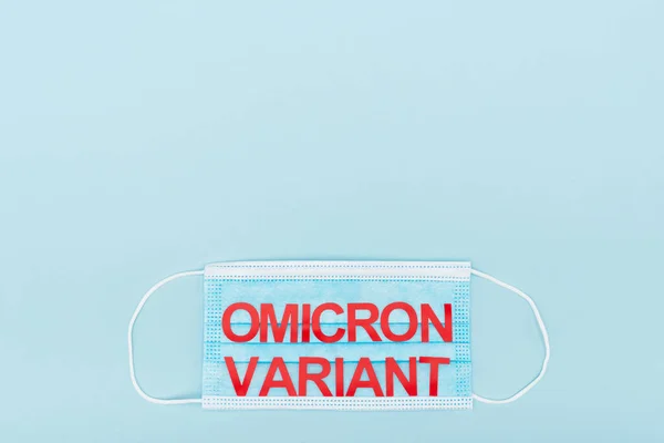 Top view of medical mask with red omicron variant lettering on blue background with copy space — Stock Photo