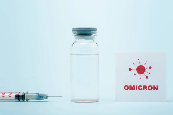 Syringe, vaccine vial and card with omicron lettering and bacteria icon on blue - foto de stock