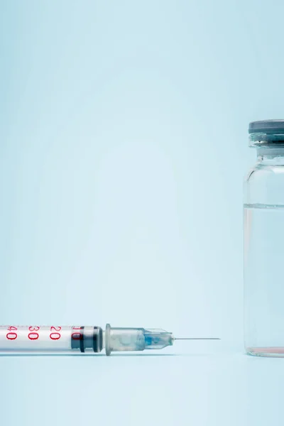 Close up view of vaccine bottle near syringe on blue background, omicron variant concept — стоковое фото