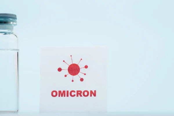 Vaccine vial near card with omicron lettering and bacteria icon on blue background — Photo de stock