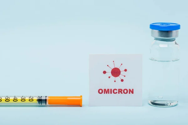 Card with omicron lettering near syringe and vaccine vial on blue background - foto de stock