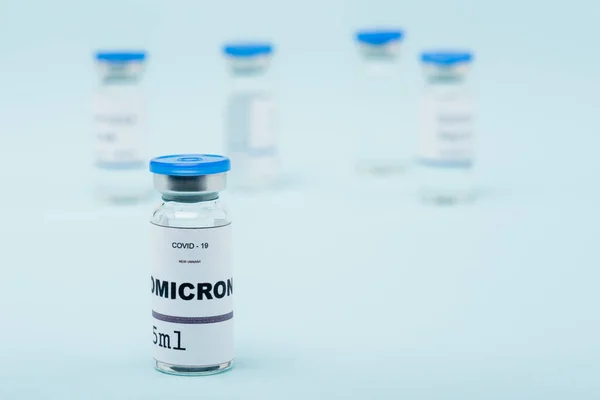 Selective focus of covid-19 omicron variant vaccine near blurred vials on blue — Stock Photo