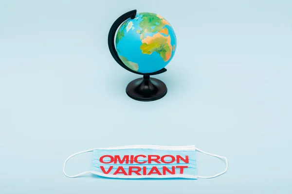 Medical mask with red omicron variant lettering near globe on blue background - foto de stock