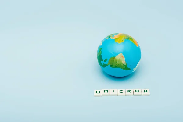 White cubes with omicron lettering near globe on blue background with copy space - foto de stock