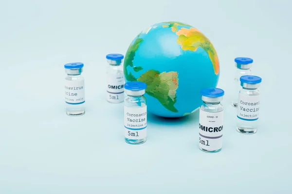 Covid-19 omicron variant vaccine bottles near globe on blue background — Stock Photo