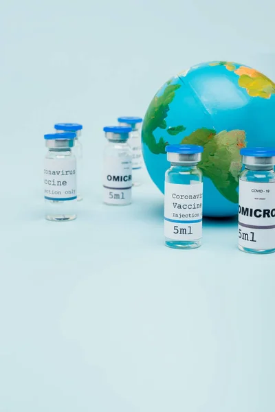 Covid-19 and omicron strain vaccine jars near globe on blue — Stockfoto
