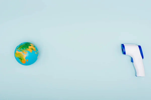 Вид зверху безконтактного термометра поблизу глобуса на синьому фоні з простором для копіювання — стокове фото