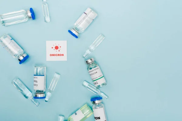 Top view of vaccine vials and ampoules near card with omicron lettering and bacteria on blue - foto de stock