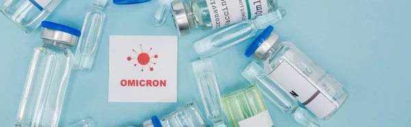 Top view of card with red omicron lettering and bacteria icon near vaccine bottles and ampoules on blue, banner — Photo de stock