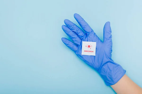 Vista recortada del médico en guante de látex con tarjeta blanca con letras de omicrón rojo y bacterias en azul - foto de stock