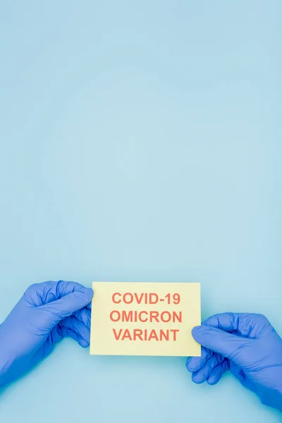 Cropped view of doctor in latex gloves holding card with red covid-19 omicron variant lettering on blue — Foto stock