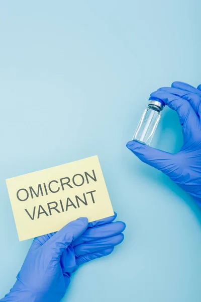 Partial view of doctor with vaccine vial and card with omicron variant lettering on blue — Fotografia de Stock