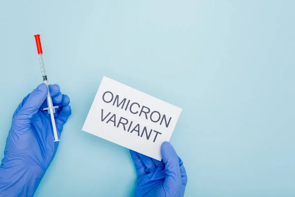 Cropped view of doctor holding syringe and card with omicron variant lettering on blue — Fotografia de Stock