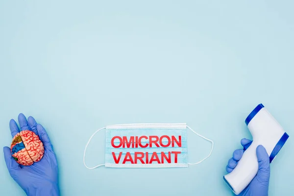 Partial view of scientist with brain model and pyrometer near medical mask with red omicron lettering on blue — Stock Photo
