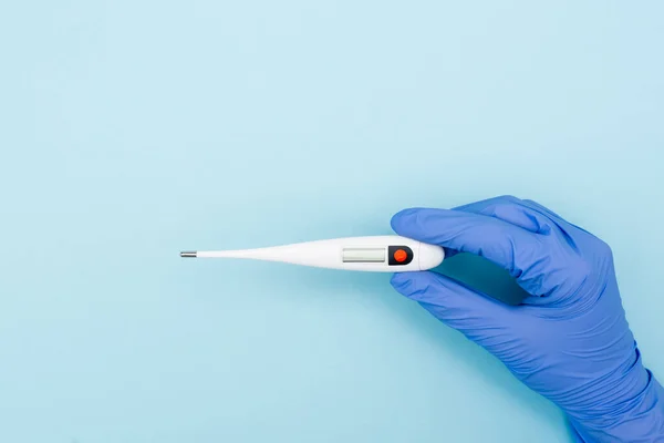 Partial view of doctor in latex glove holding electronic thermometer on blue — Stock Photo