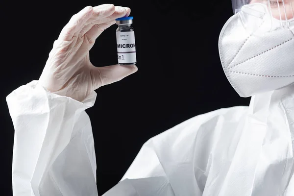 Partial view of doctor in medical mask and hazmat suit holding covid-19 omicron variant vaccine isolated on black — Stock Photo