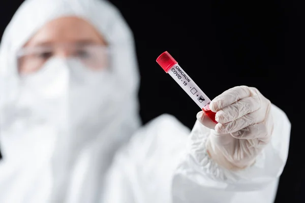 Científico borroso en traje de hazmat blanco con prueba positiva de variante omicrónica covid-19 aislada en negro - foto de stock