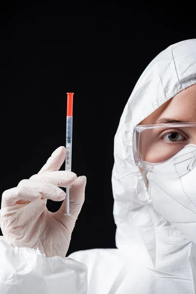 Partial view of doctor in white hazmat suit holding syringe isolated on black — стоковое фото