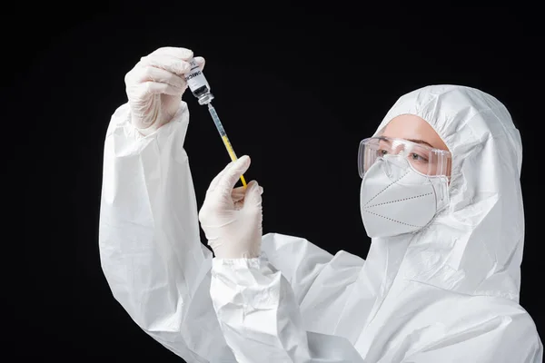 Inmunólogo en equipo de protección personal con jeringa y vacuna covid-19 de variante omicrónica aislada en negro - foto de stock
