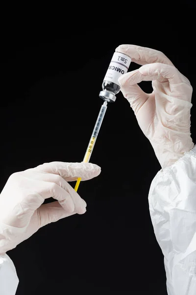 Partial view of immunologist in white latex gloves holding syringe and omicron variant vaccine isolated on black — стоковое фото