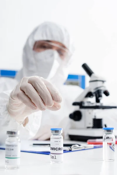 Vials with covid-19 omicron vaccine near blurred doctor working near microscope in lab — Stock Photo