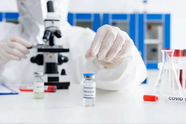 Cropped view of blurred scientist working with microscope near coronavirus vaccine and test tubes — Foto stock