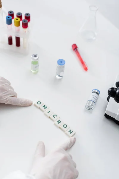 Partial view of immunologist in latex gloves near cubes with omicron lettering, vaccine vials and test tubes in lab — Fotografia de Stock