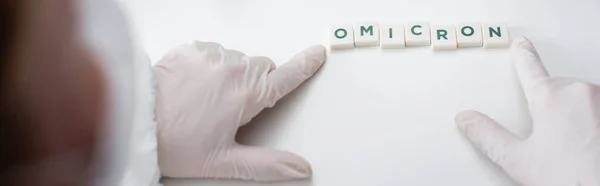 Cropped view of blurred doctor near cubes with omicron lettering on desk, banner — Stock Photo