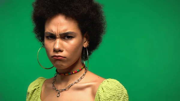 Femme afro-américaine frustrée fronçant les sourcils et regardant la caméra isolée sur vert — Photo de stock