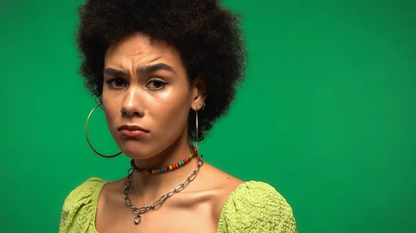 Sad african american woman frowning and looking at camera isolated on green — Stockfoto