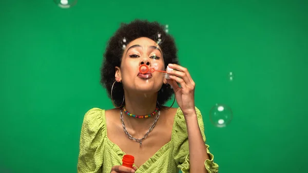 Young african american woman blowing soap bubbles isolated on green — Fotografia de Stock