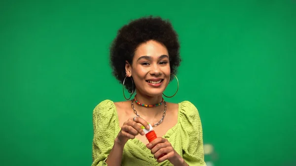 Gaie femme afro-américaine tenant bouteille et baguette à bulles isolée sur vert — Photo de stock