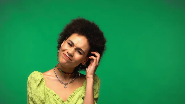 Mujer afroamericana confusa arañando la cabeza y mirando a la cámara aislada en verde - foto de stock