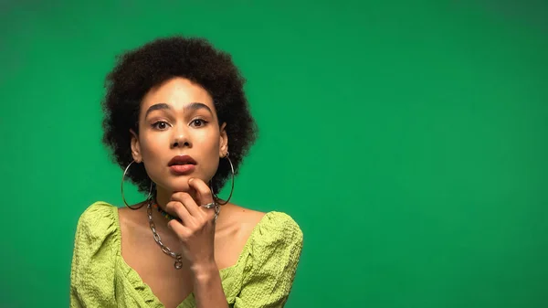 Mujer afroamericana pensativa mirando la cámara aislada en verde - foto de stock