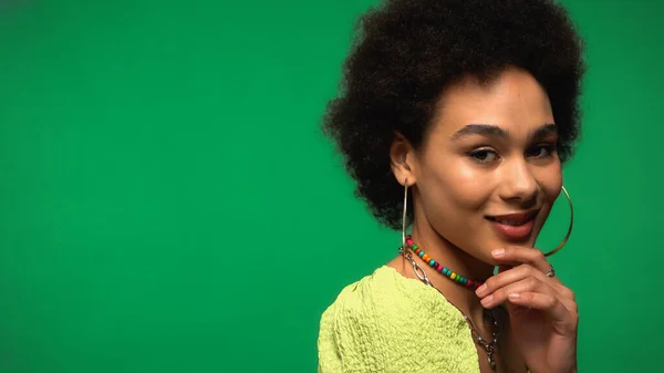 Erfreut afrikanisch-amerikanische Frau mit Reifen Ohrringe Blick in die Kamera isoliert auf grün — Stockfoto