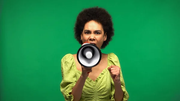 Furiosa mujer afroamericana gritando en megáfono y mirando a la cámara aislada en verde - foto de stock