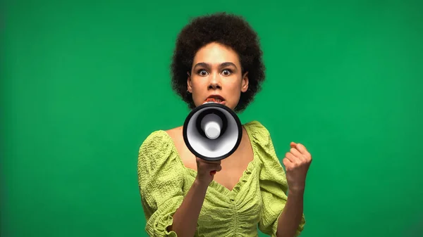 Irritated african american woman protesting while holding loudspeaker and looking at camera isolated on green — стоковое фото