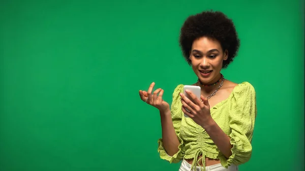 Sorrindo mulher afro-americana usando smartphone isolado no verde — Fotografia de Stock